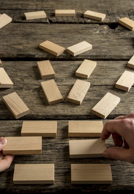 Business teamwork and bright ideas concept with a group of business people arranging wooden blocks into the shape of a light bulb on an old rustic table, close up view of their hands.